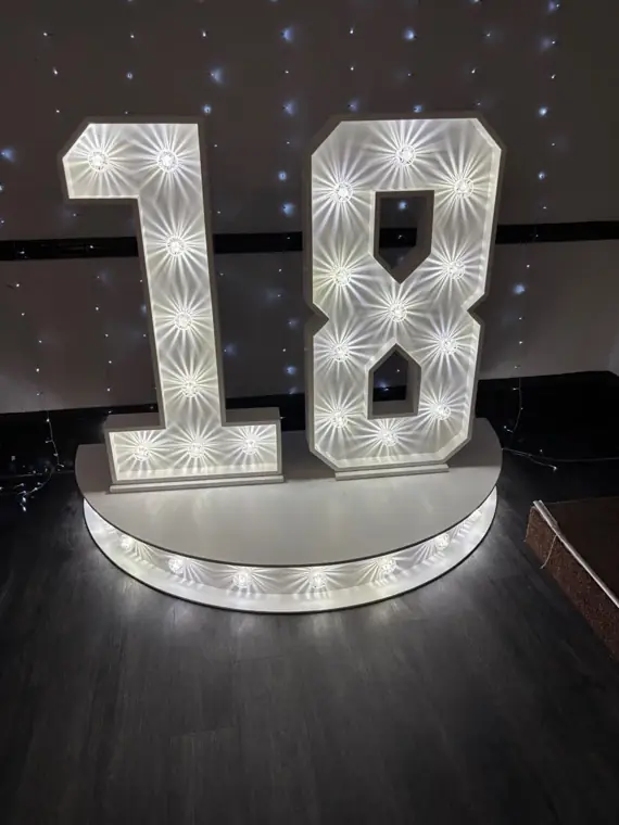 Giant illuminated 4ft LED marquee 18 numbers on a curved plinth in front of a fairy-light backdrop for an 18th birthday party
