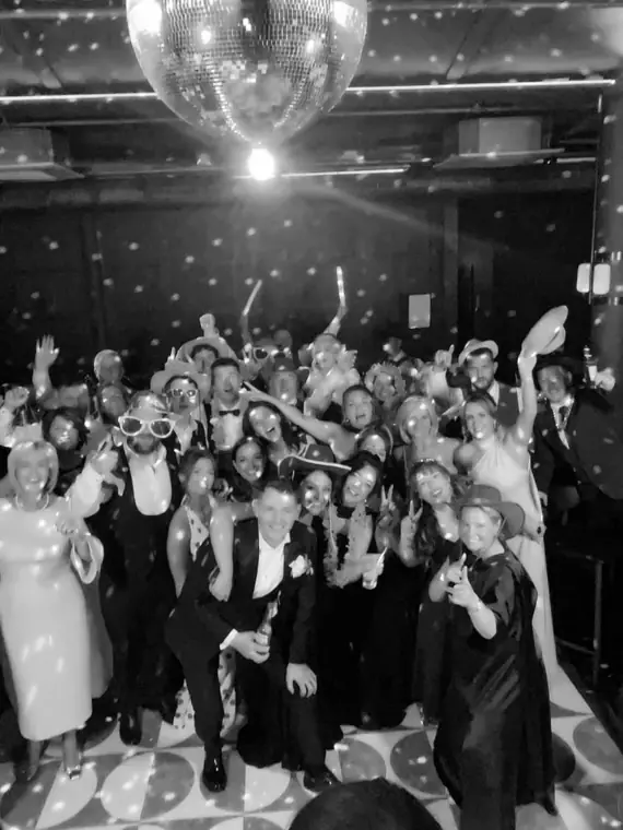 Black-and-white 360 video booth still of a large wedding party crowded under a mirrorball on the dance floor