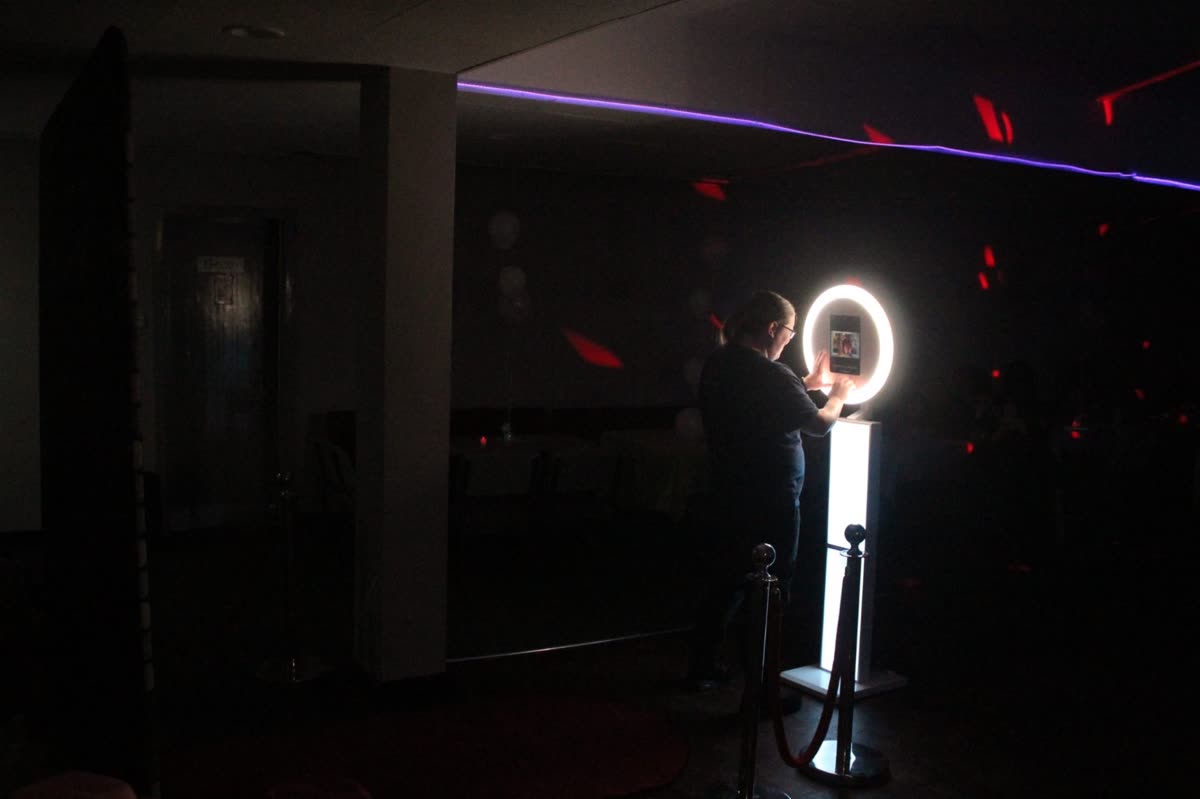 Attendant operating a Halo ring-light selfie booth in a darkened function suite with red and purple party lighting