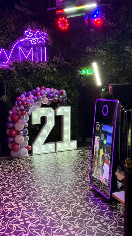 Magic Mirror photo booth with purple neon frame beside illuminated 4ft LED 21 numbers and a balloon arch at an Ivy Mill 21st birthday party