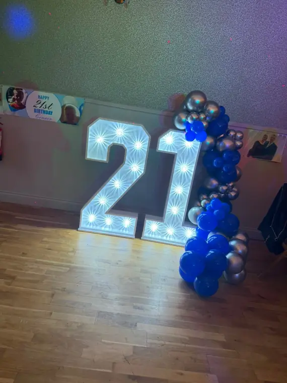 Illuminated 4ft LED marquee 21 numbers with a blue and silver balloon garland at a 21st birthday party