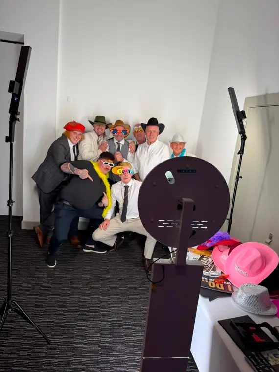 Wedding guests in hats and novelty sunglasses crowding together for a group shot at the Halo selfie booth