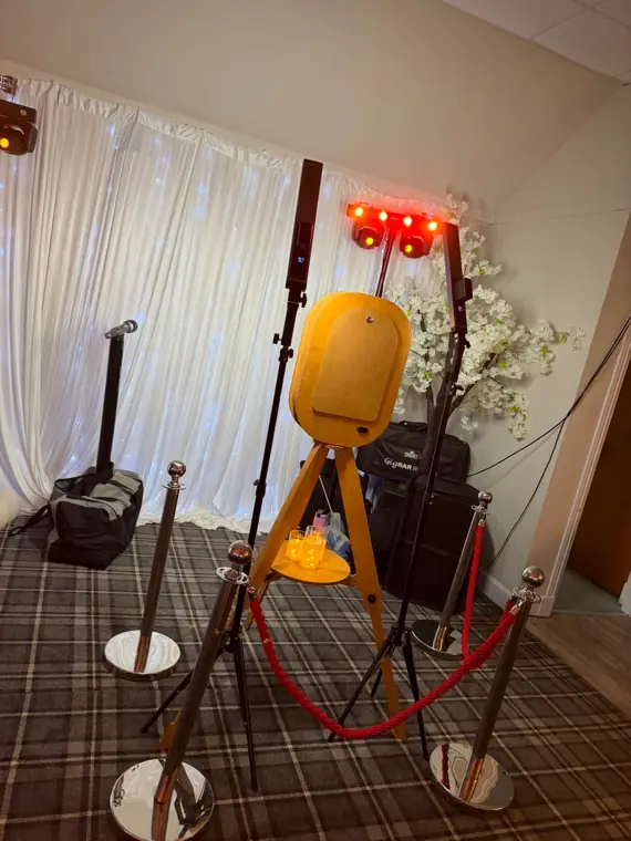Vintage rustic photo booth with red rope barrier in front of a white fairy-light drape backdrop and party lighting at a Scottish function suite
