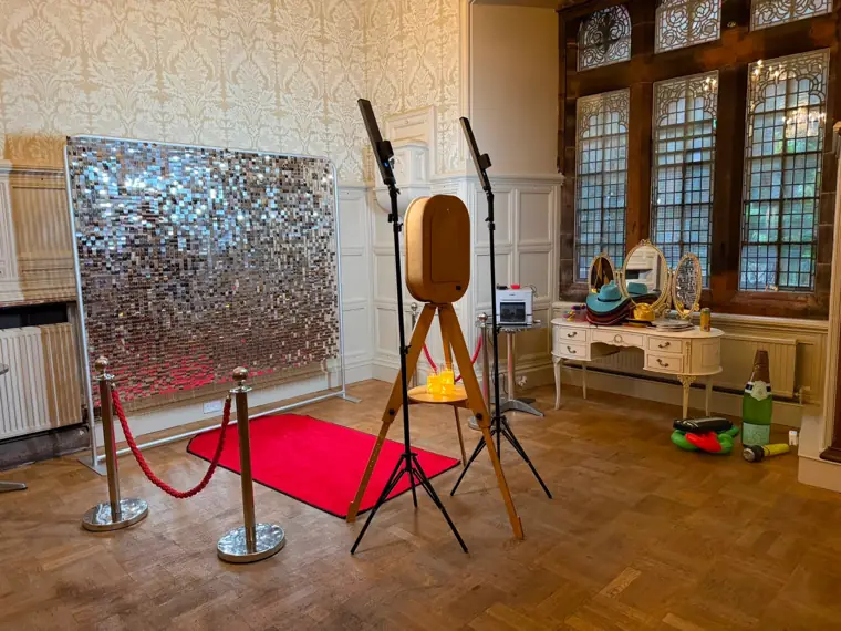 Vintage rustic photo booth with silver sequin shimmer wall, red carpet and prop table in a wood-panelled manor house wedding room