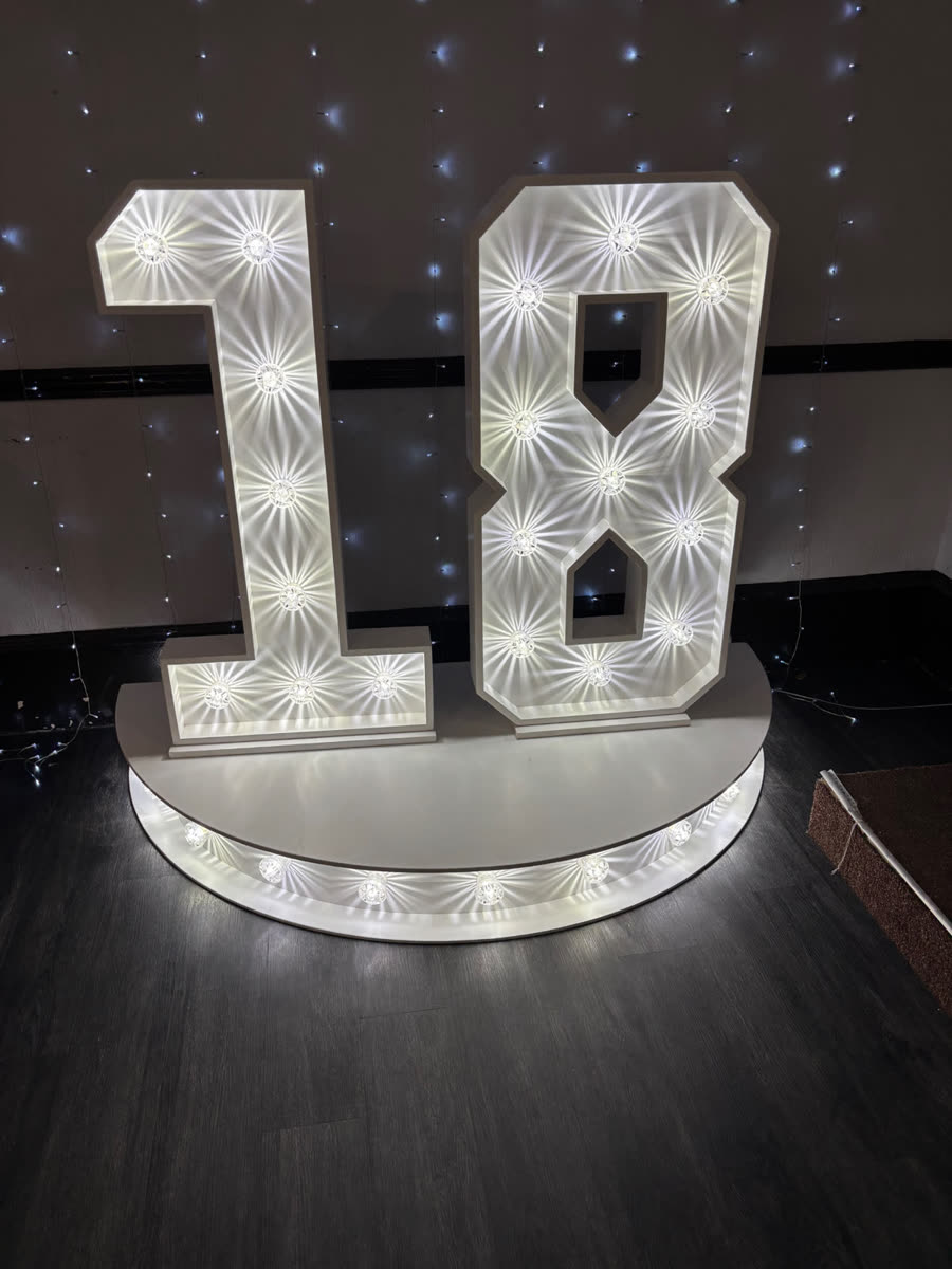Giant illuminated 4ft LED marquee 18 numbers on a curved plinth in front of a fairy-light backdrop for an 18th birthday party