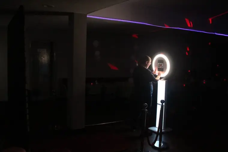 Attendant operating a Halo ring-light selfie booth in a darkened function suite with red and purple party lighting